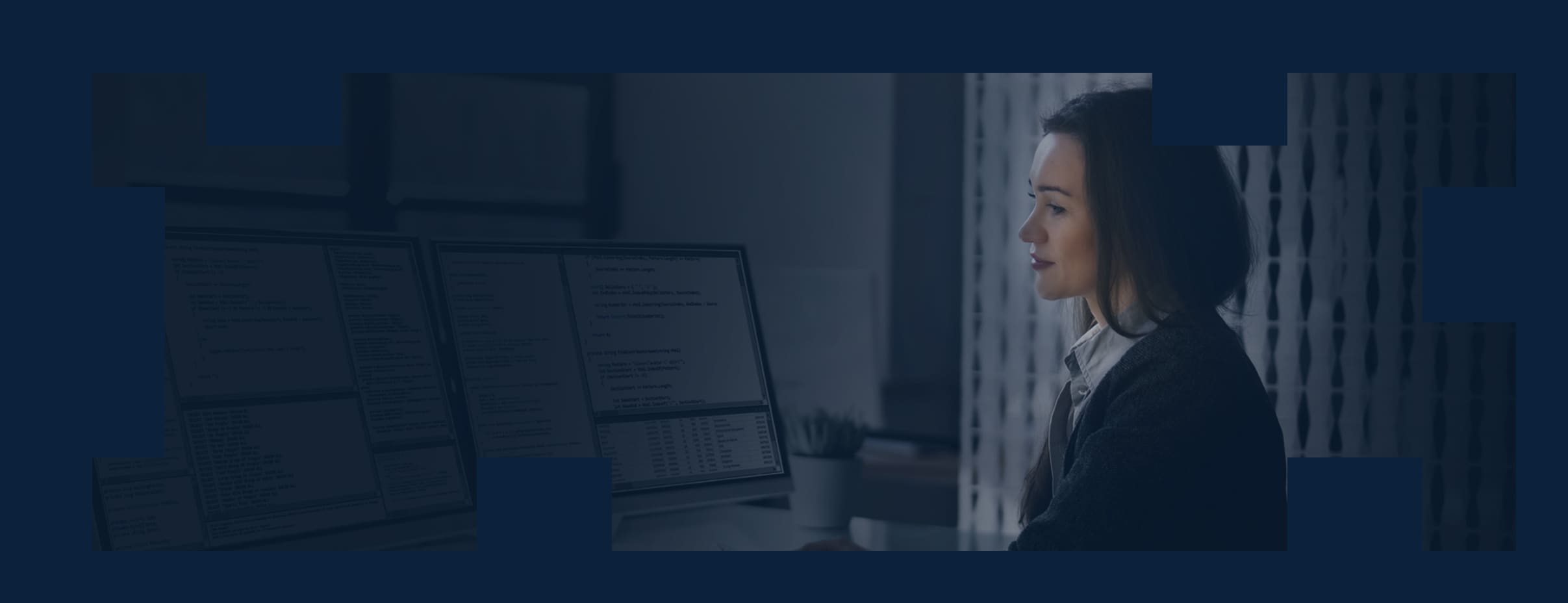 A young professional at work looking at data reports on multiple large monitors