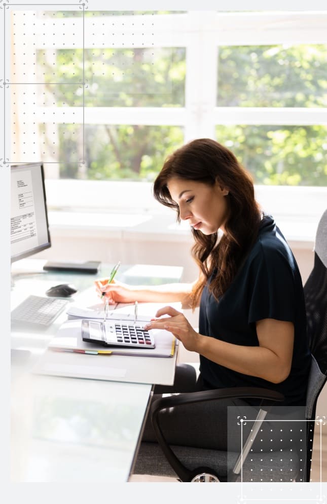 A young professional at work punching numbers into a calculator in a bright sunny office