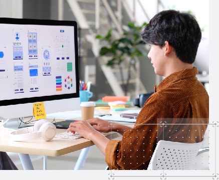 A young professional sitting at his desk with a to-go coffee and headphones working on design files